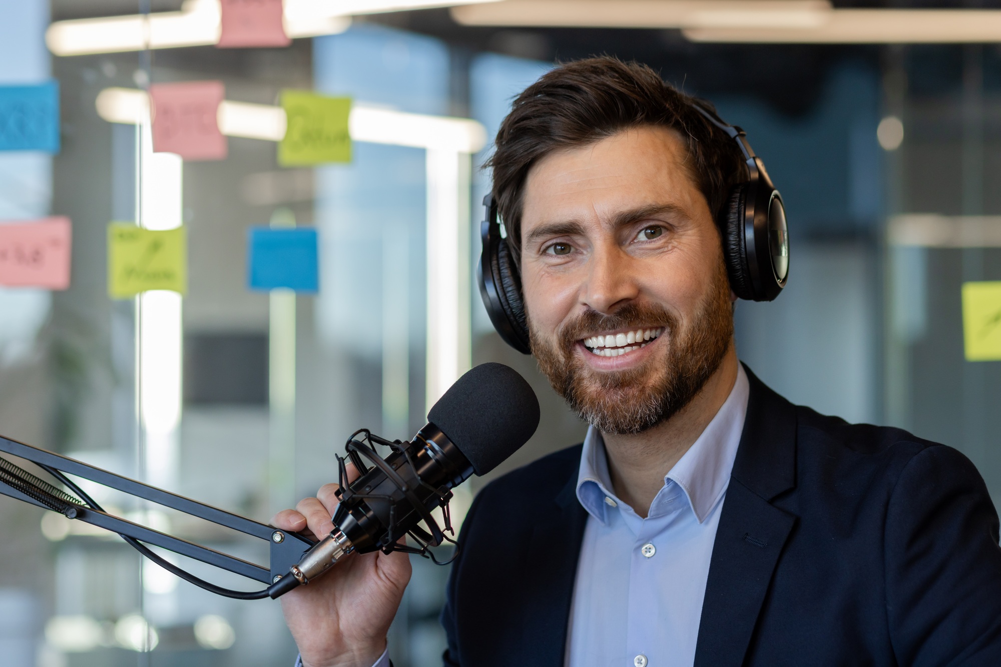 Confident podcast host wearing headphones while recording in office studio with microphone setup